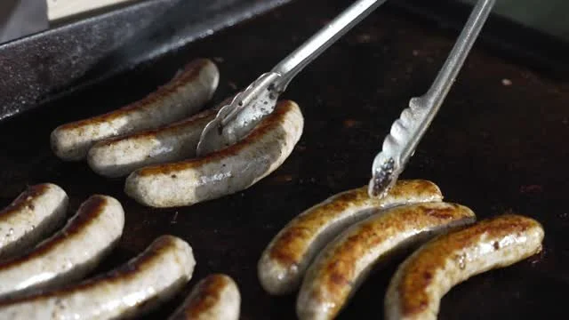 Bratwurst being turned on the grill with tongs.