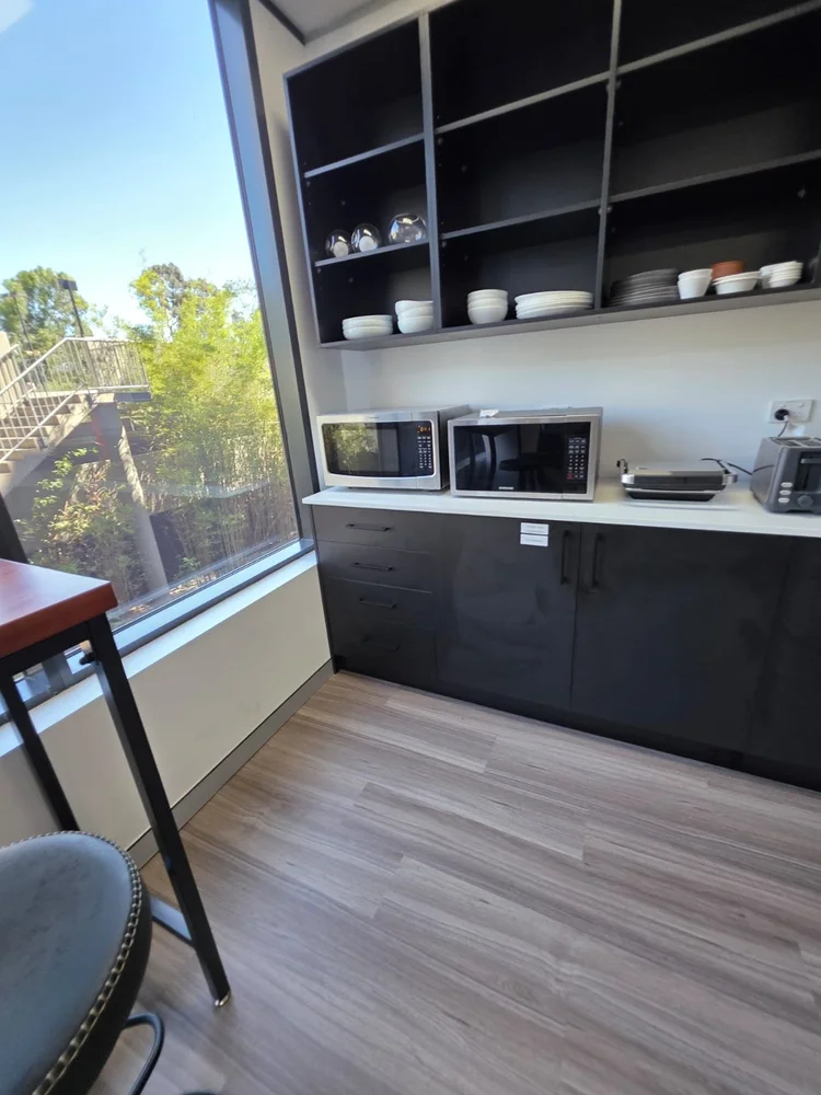 The finished kitchenette in daily use, with crockery on open black shelves and appliances on the stone benchtop