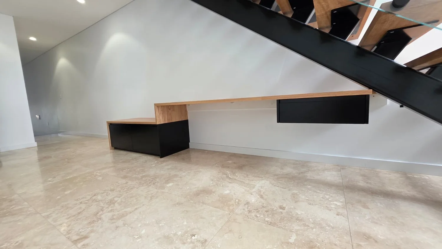 Finished under-stair joinery seen from the far end of the room, floating drawer box beneath the lowest stair run