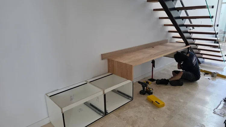 Installer fixing the floating desk beneath the staircase, laser level and tools on the floor