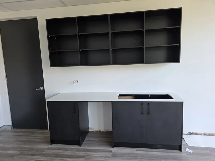 Kitchenette mid-installation: black cabinets topped in white stone, sink cutout open, tap roughed into the wall