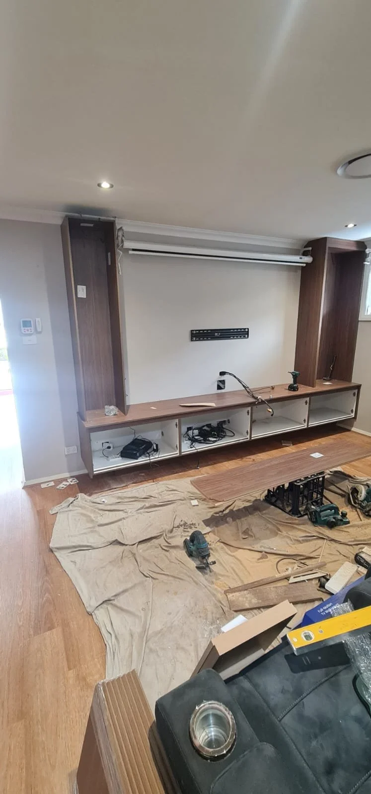 Mid-install: carcasses open and levelled, TV bracket on the bare wall, drop sheets down