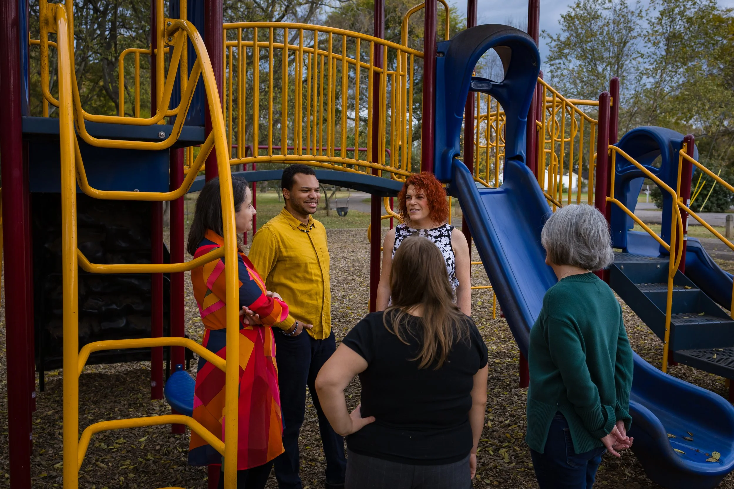 Five adults talking beside colorful playground equipment.