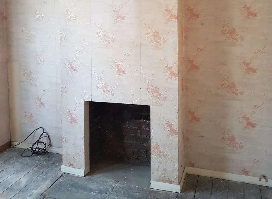 Before: the living room fireplace opening, bare brick and peeling wallpaper