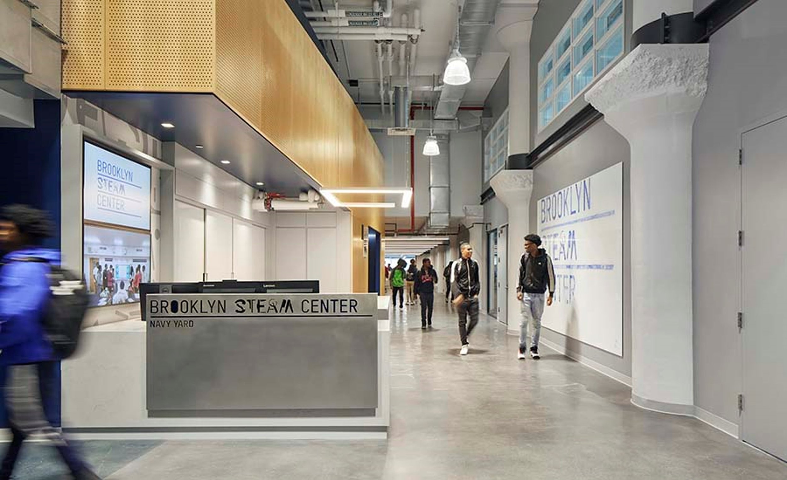 A photo of the Brooklyn steam center building lobby/entrance showing the front desk with the center’s name on it with people walking the hallway. Courtesy of the Brooklyn Navy Yard Development Corporation.