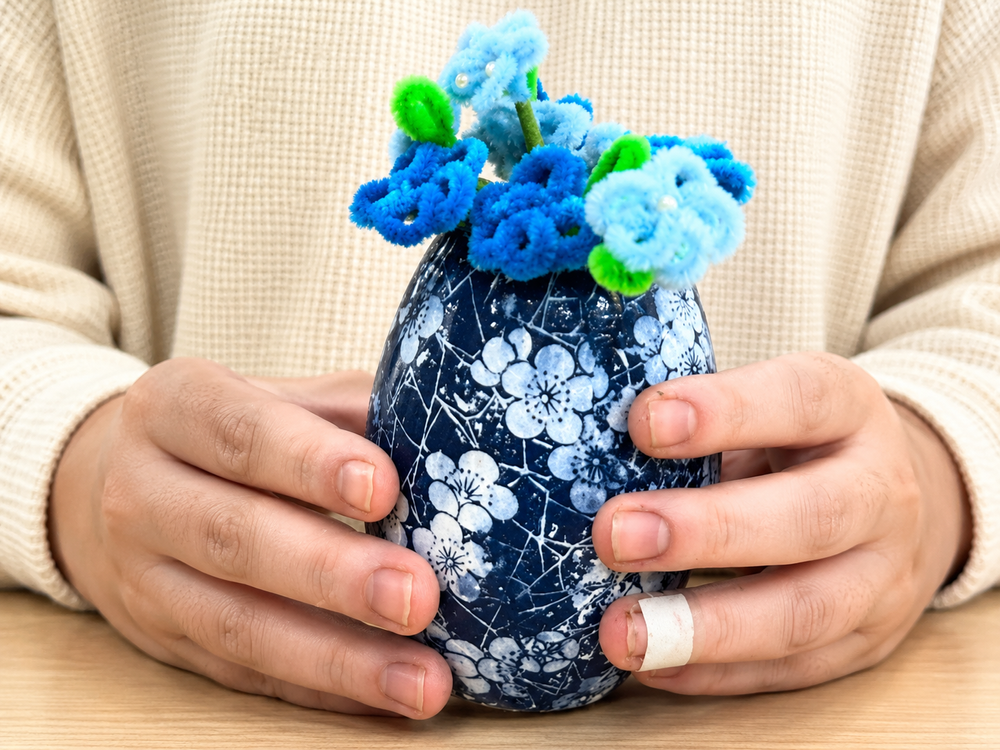 Hands holding a blue floral patterned vase with handmade pipe cleaner flowers for a pattern making craft programme