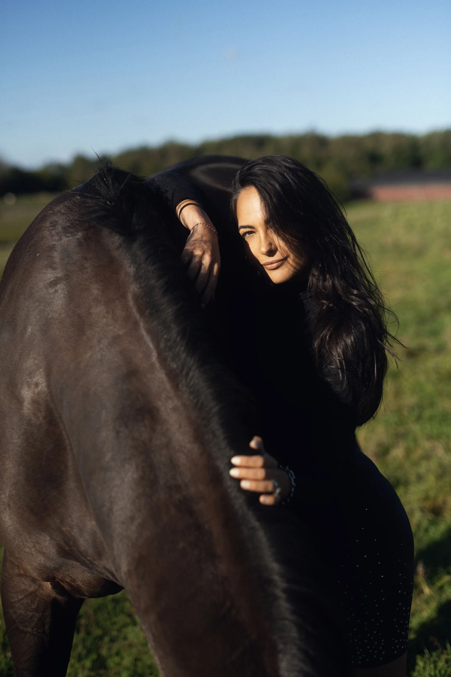 Bee Bosnak leaning on a dark horse in a field