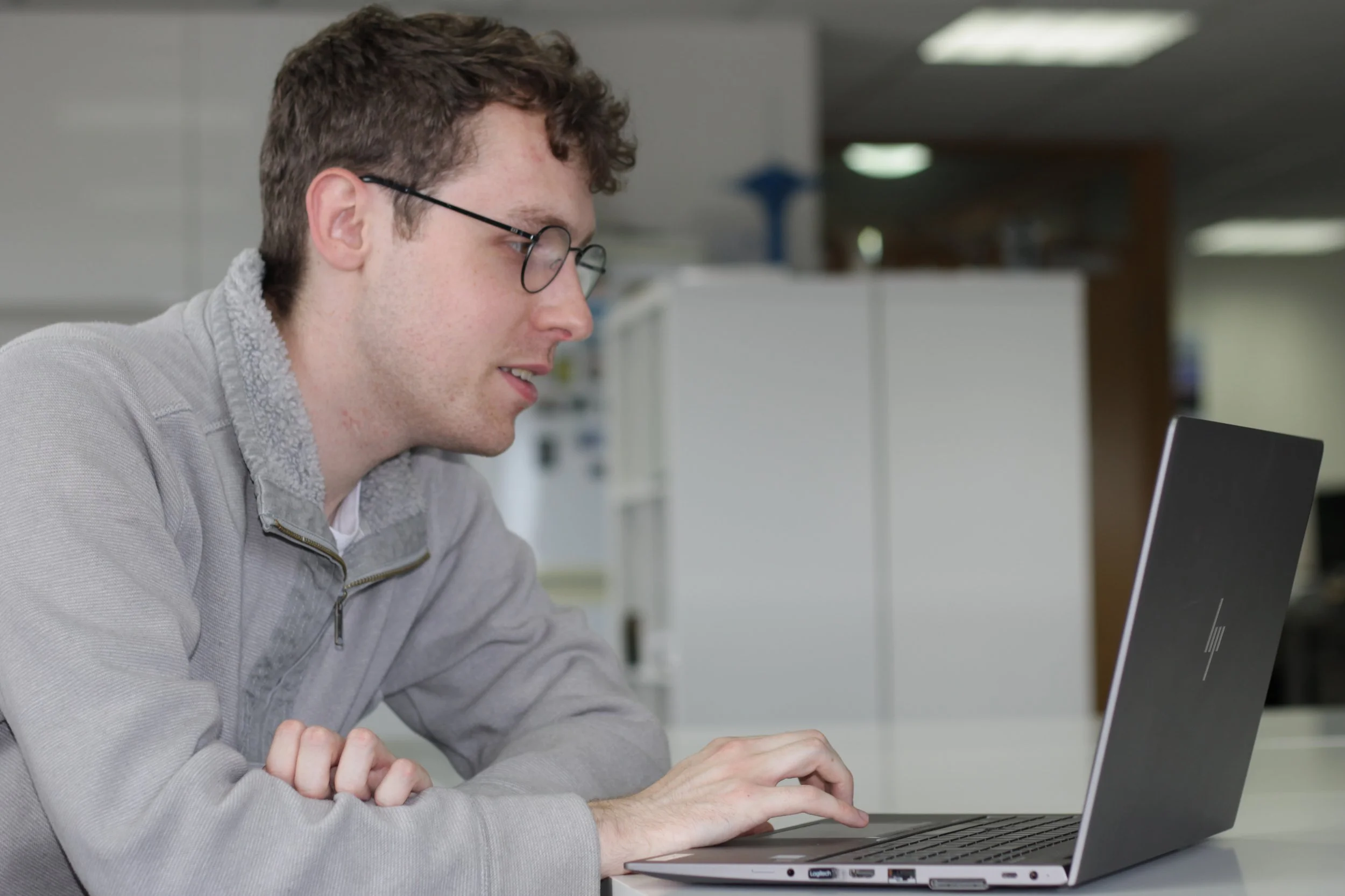 A photo of Sam Berry sat a laptop, talking to another.