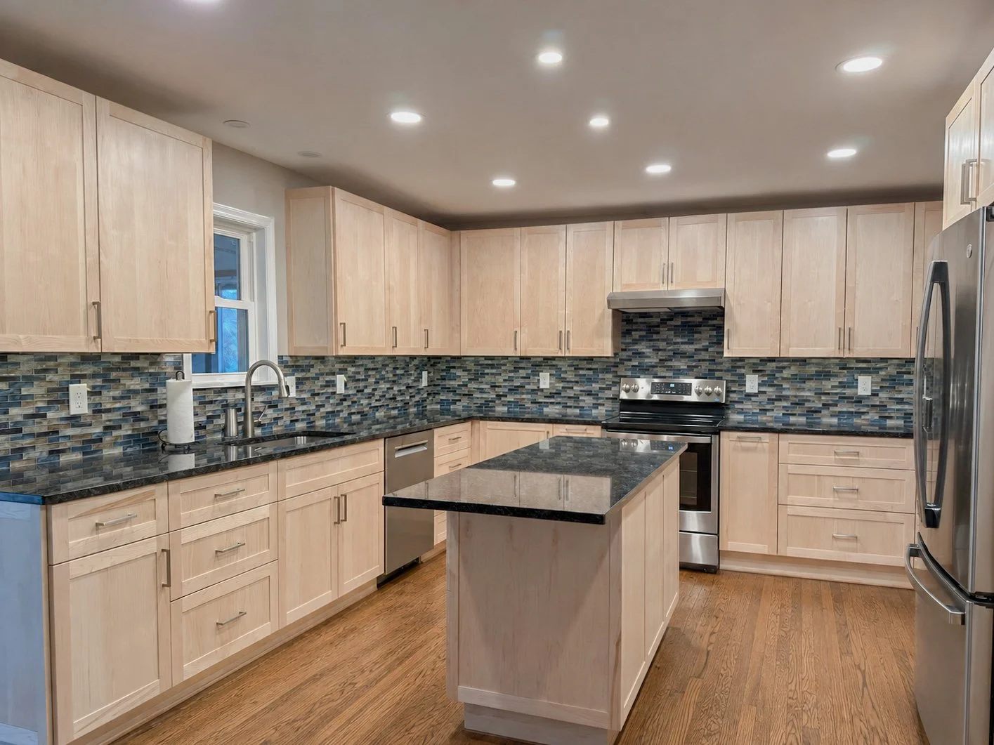 Finished Maryland kitchen with natural wood cabinetry, dark counters and blue tile backsplash
