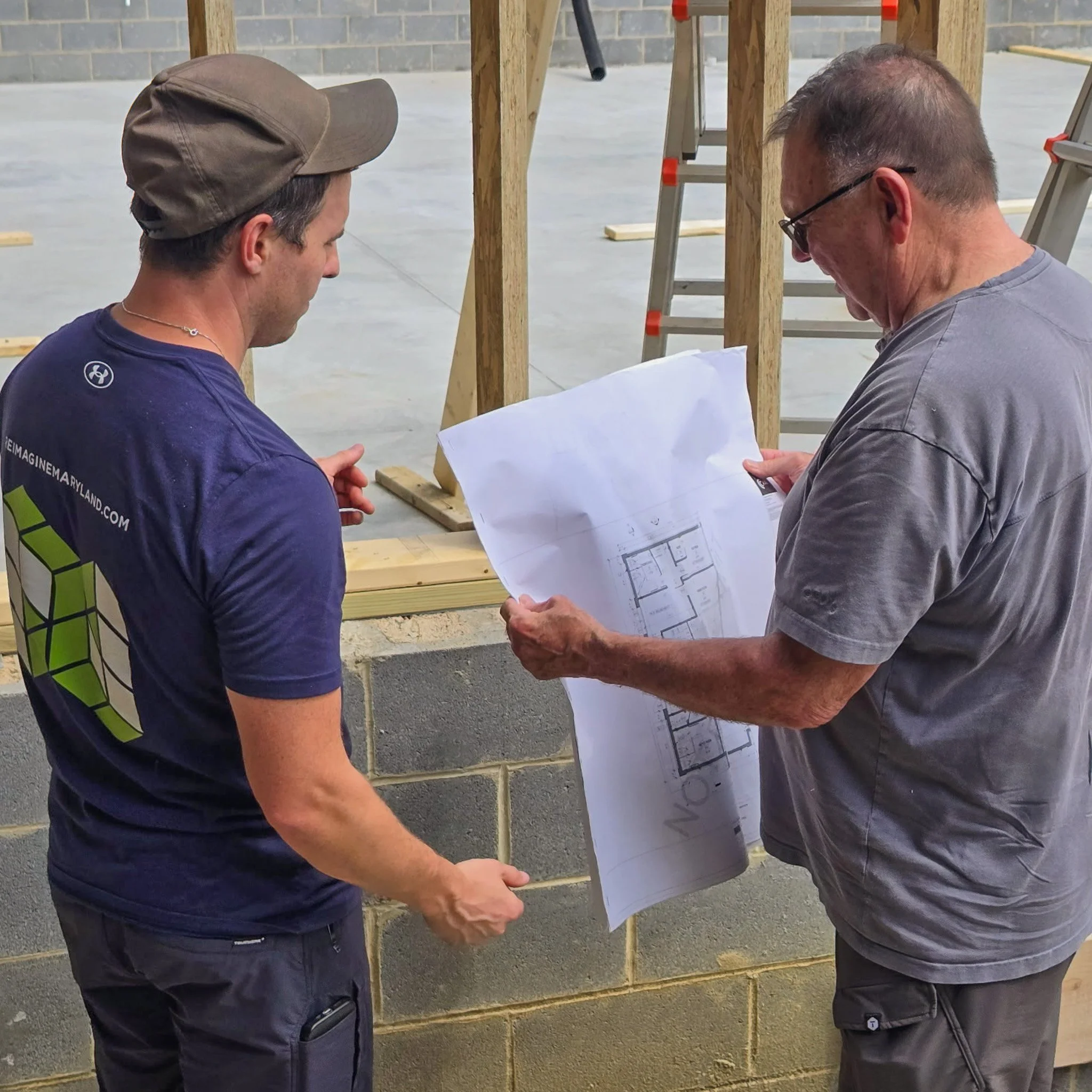 Two remodeling professionals reviewing building plans at a framed construction site