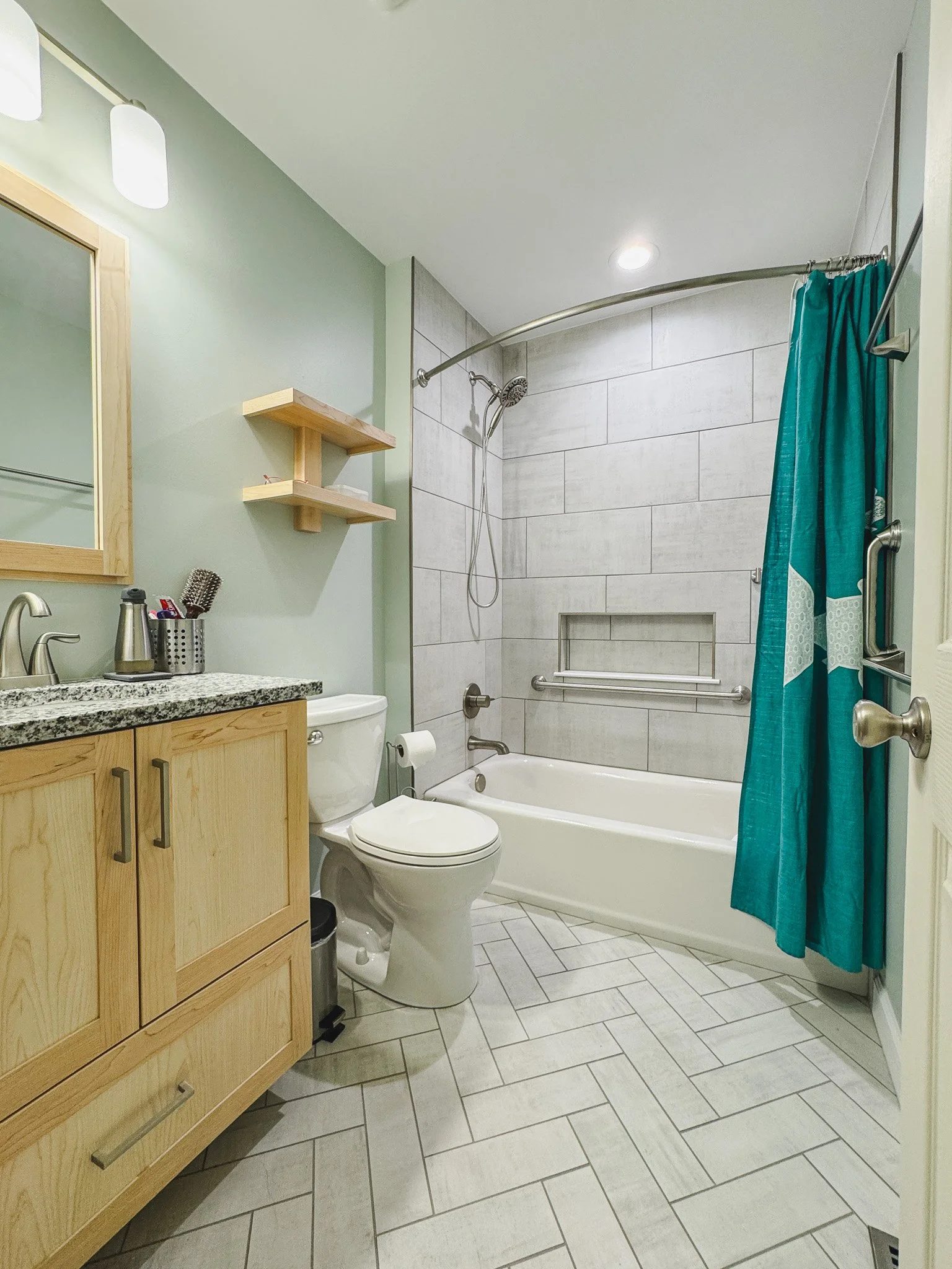 Remodeled hall bathroom in Sykesville with tiled tub surround, recessed niche, custom vanity, wood shelves, and new fixtures