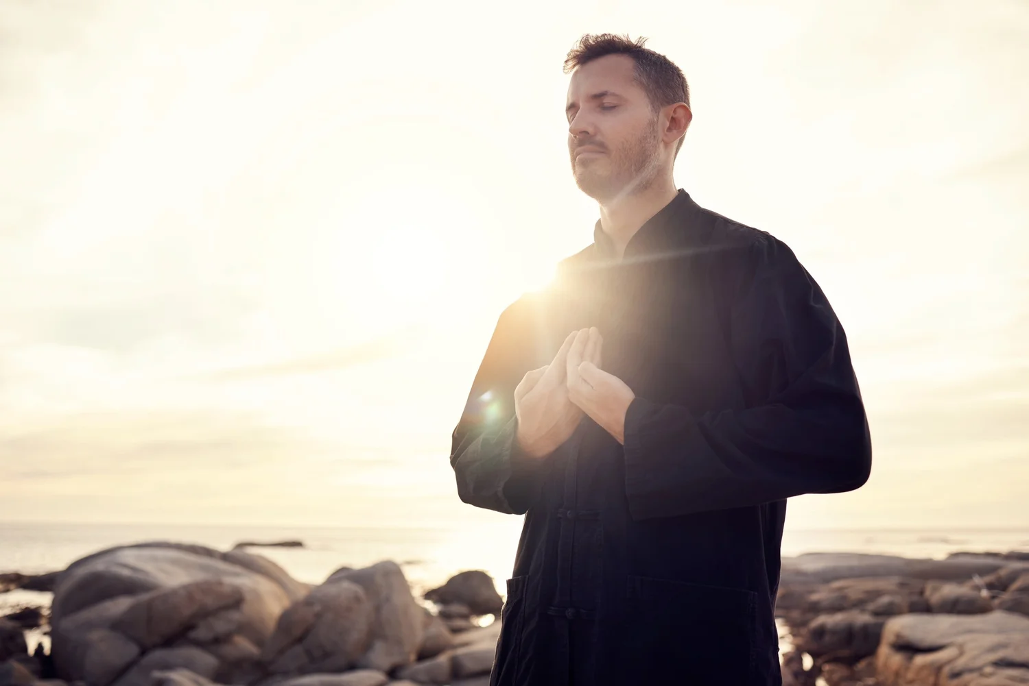 A person standing still in dark clothing, backlit by low sun