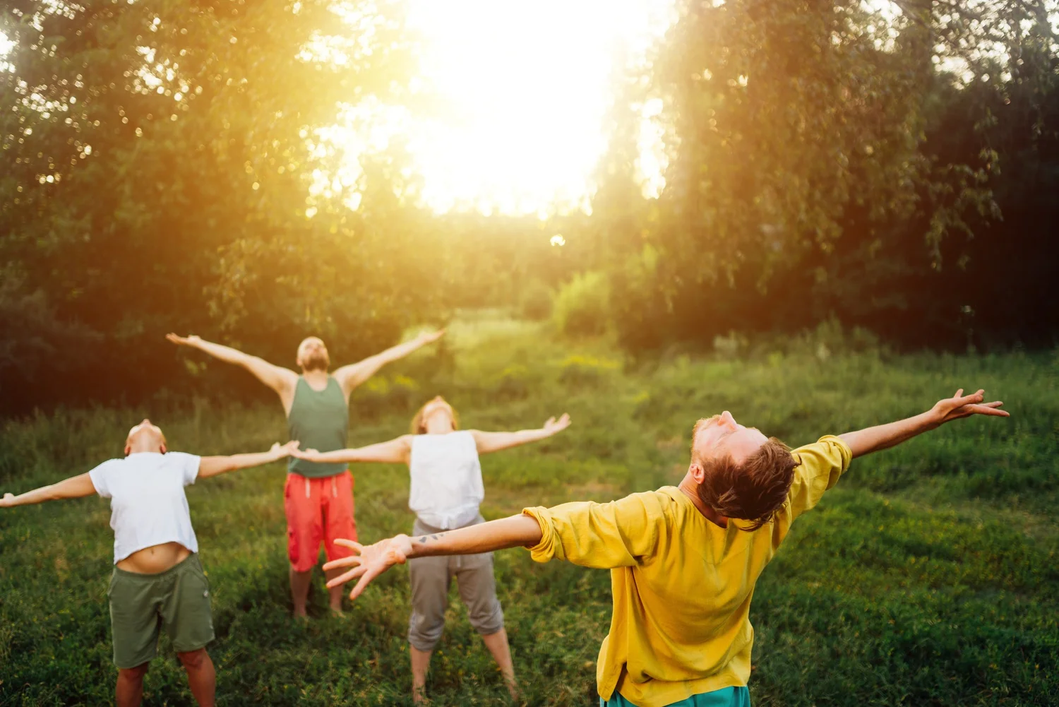 A group practising together outdoors with arms open at sunset