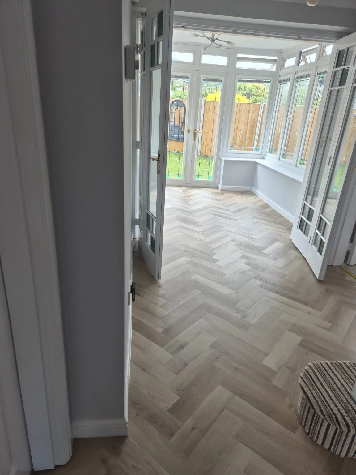 Light oak herringbone flooring leading into a bright conservatory