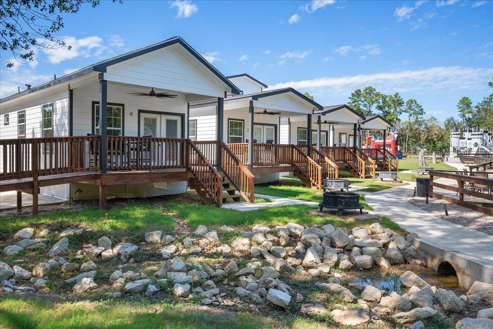 Row of white guest cabins with covered porches and fire pits