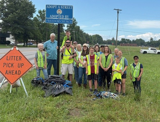 Freedom Church volunteers by the Adopt a Street sign that reads Adopted by Freedom Church