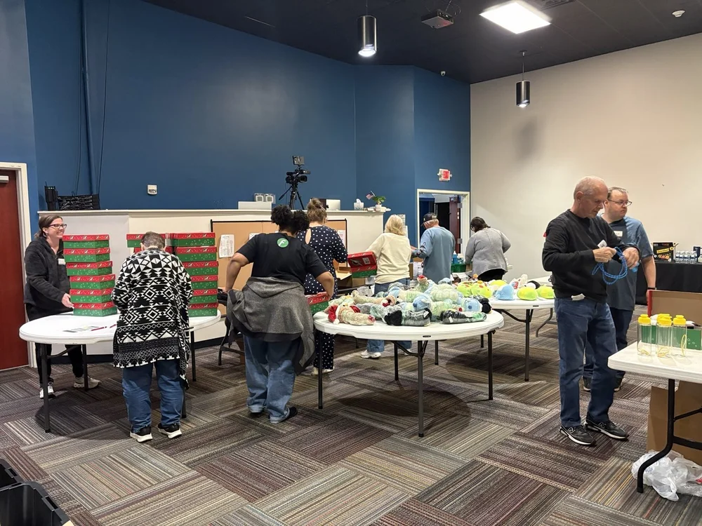Volunteers packing shoebox gifts at tables full of toys and supplies