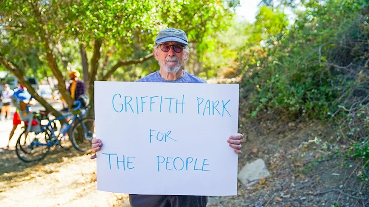 Streets Are For Everyone Volunteer in Griffith Park holding a sign stating "Griffith Park for the People."