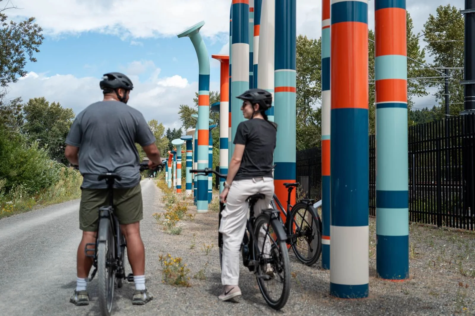 Two riders paused beside the striped art pillars on the Eastrail, wildflowers in the foreground