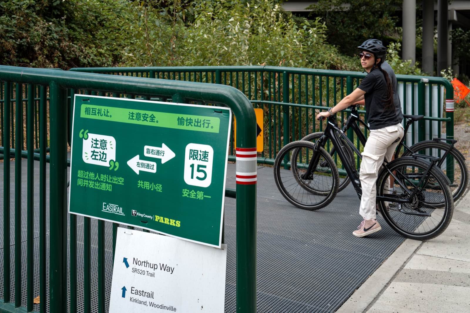 A rider stopped at an Eastrail junction sign pointing to Northup Way and the SR520 Trail one way, Kirkland and Woodinville the other