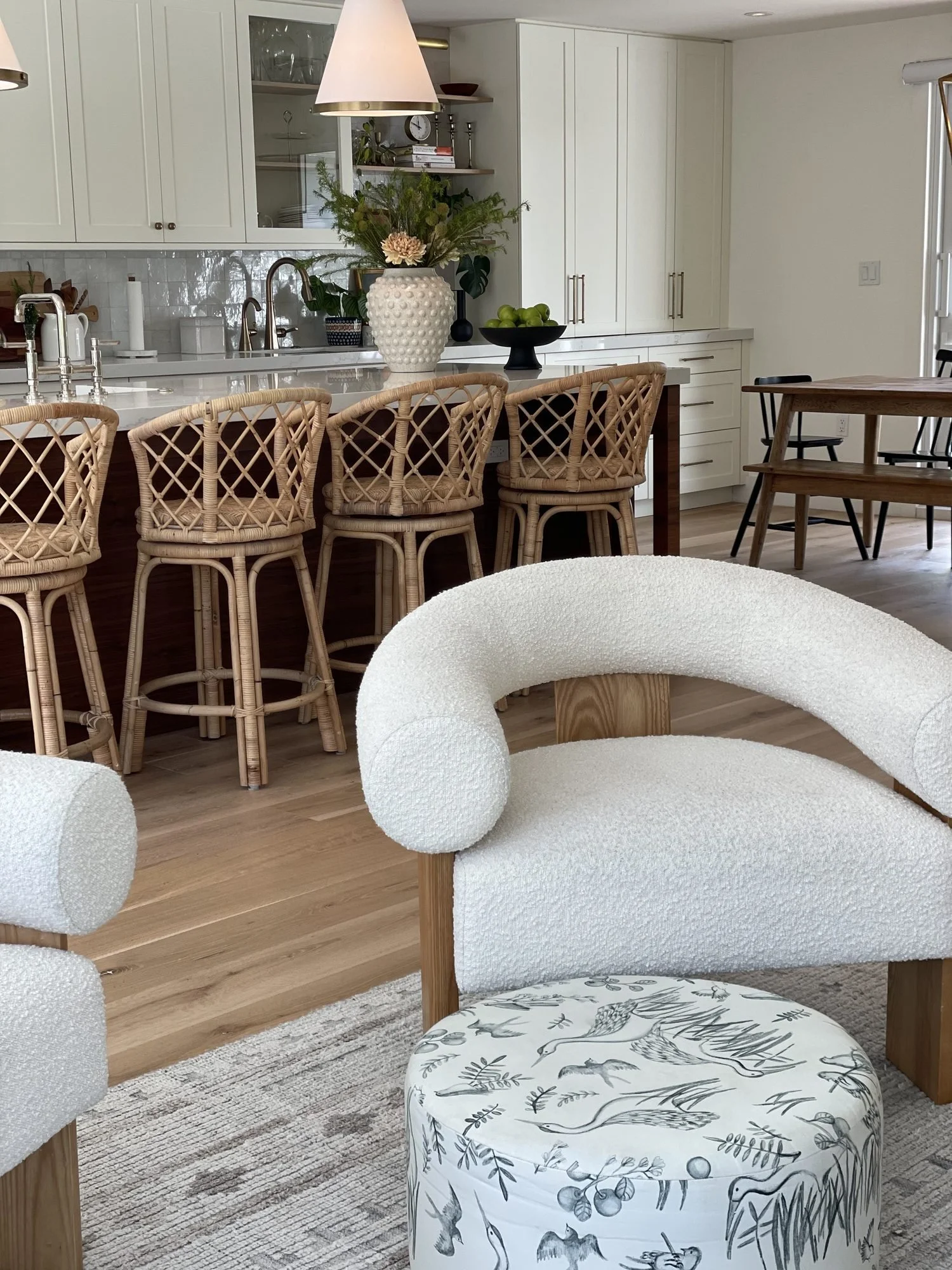 A bright kitchen and living space with rattan stools and a boucle chair