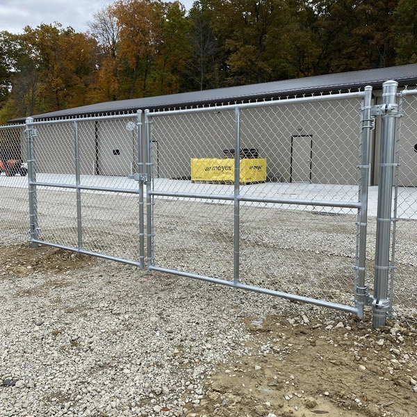 Galvanized chain-link vehicle gate and perimeter fence beside a commercial building