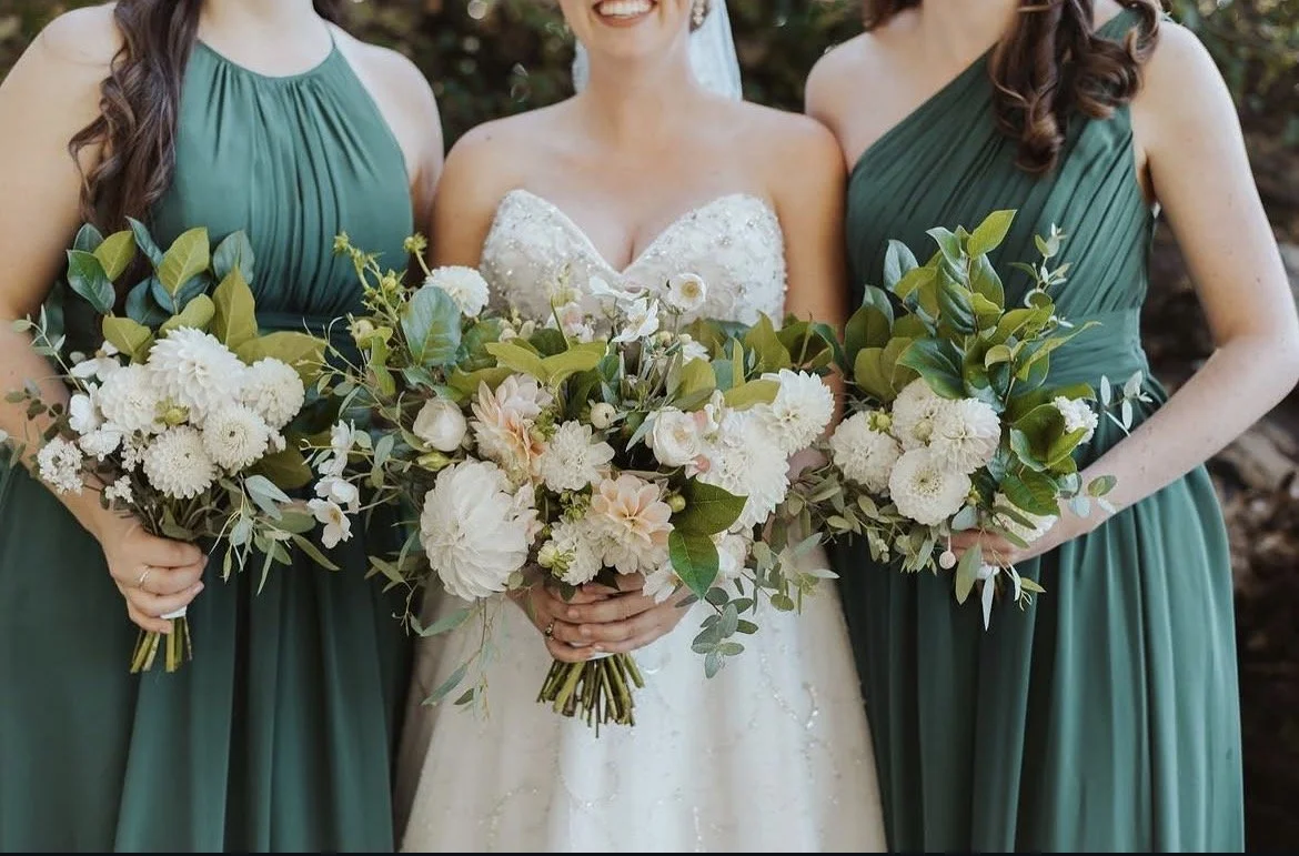 Bride and bridesmaids holding white and blush dahlia bouquets with greenery