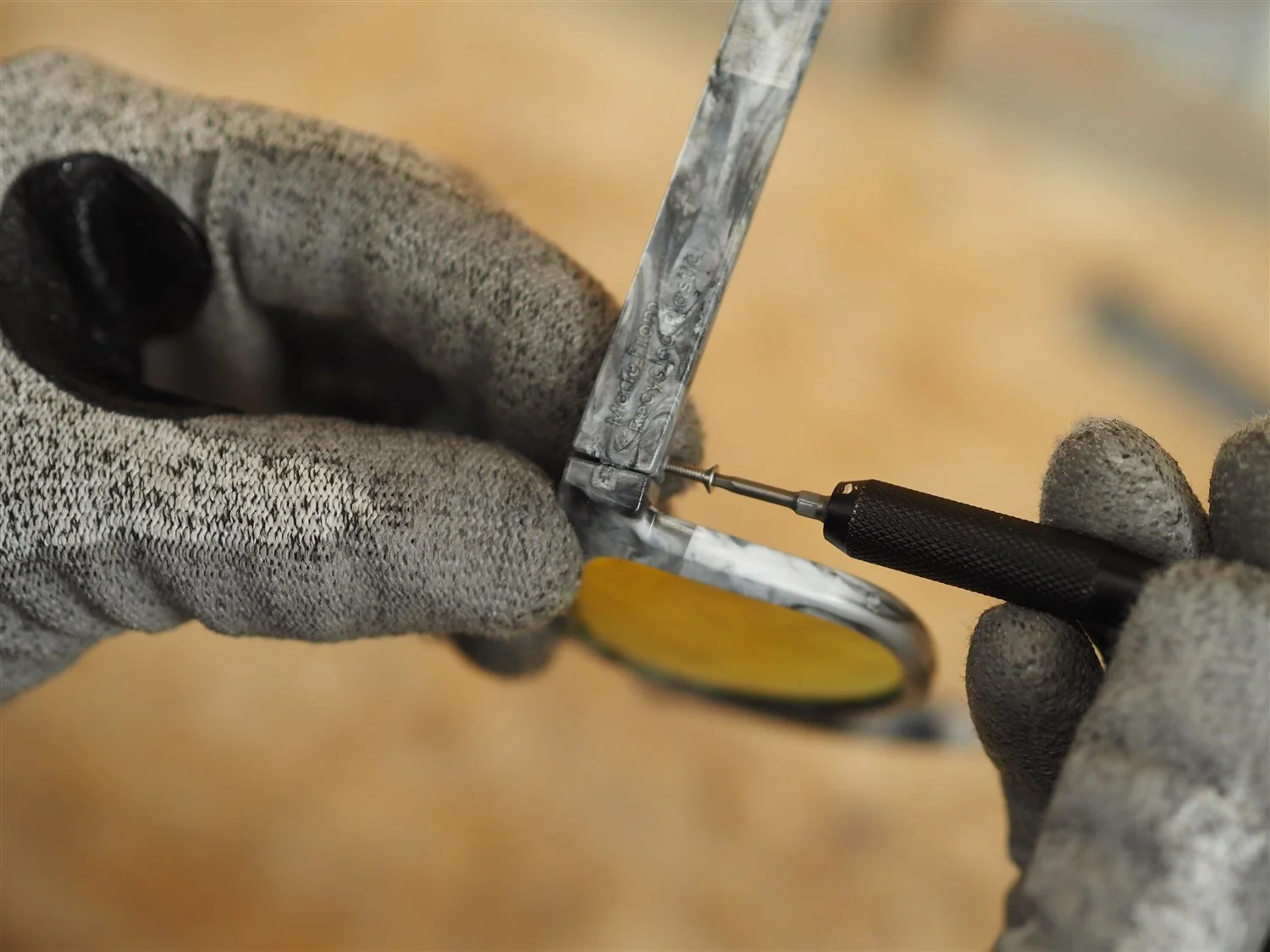 A small cross-head screwdriver driving the hinge screw through the arm into the frame, the orange lens visible below