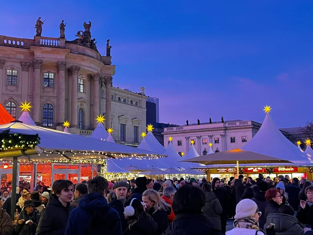 Berlin Christmas market at dusk with glowing stars, festive stalls and visitors