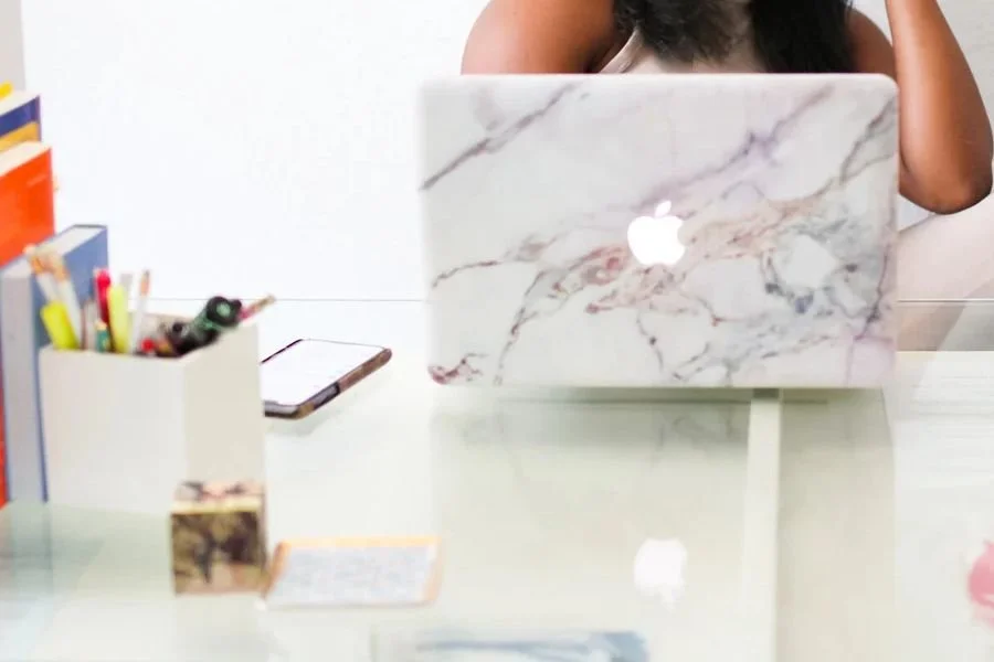 Marble laptop on a glass desk with books and supplies