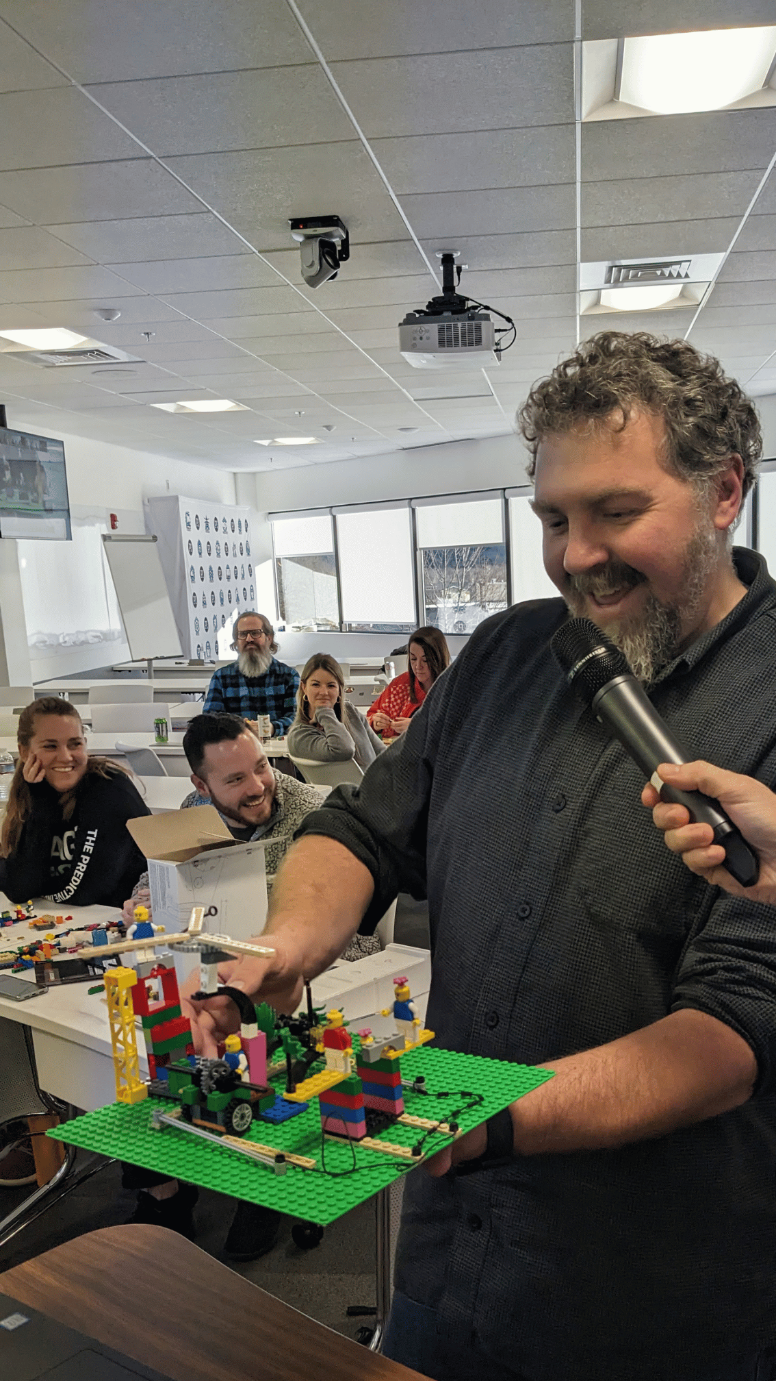 Workshop participant explaining his LEGO model to the room while colleagues listen and smile