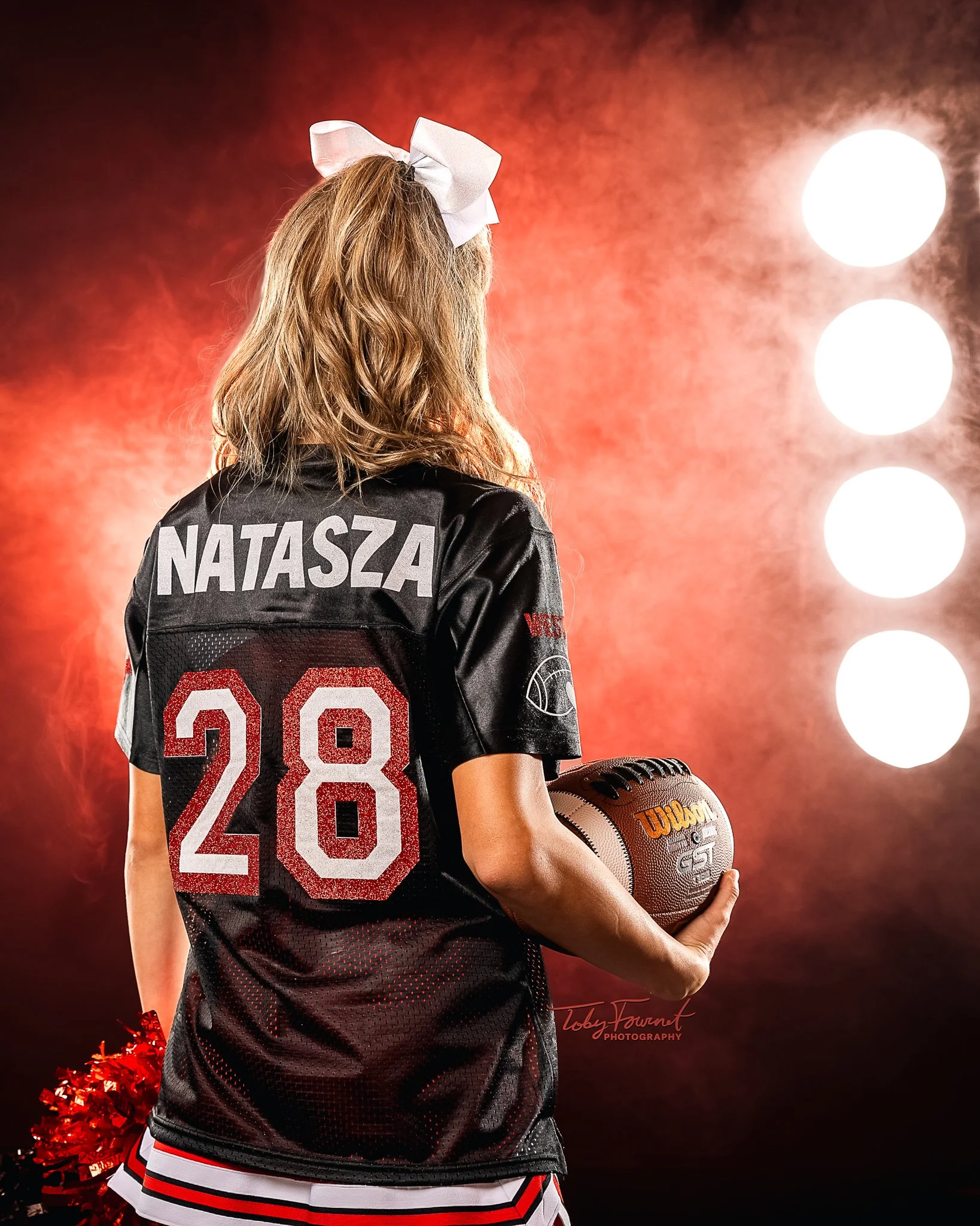 Cheer portrait from behind with a football and red lighting
