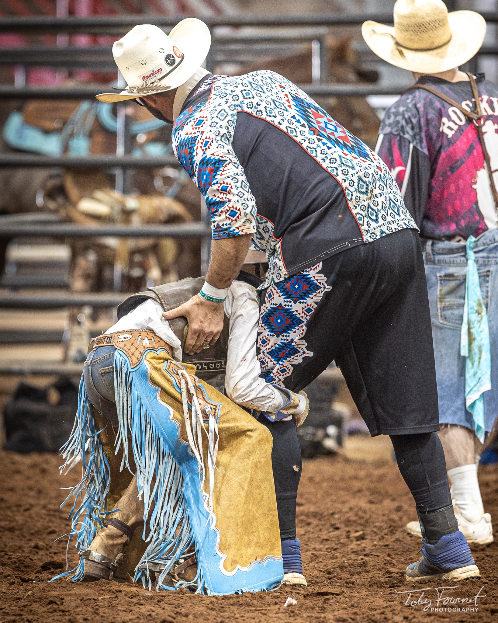Adult supporting a young rodeo rider beside the chutes