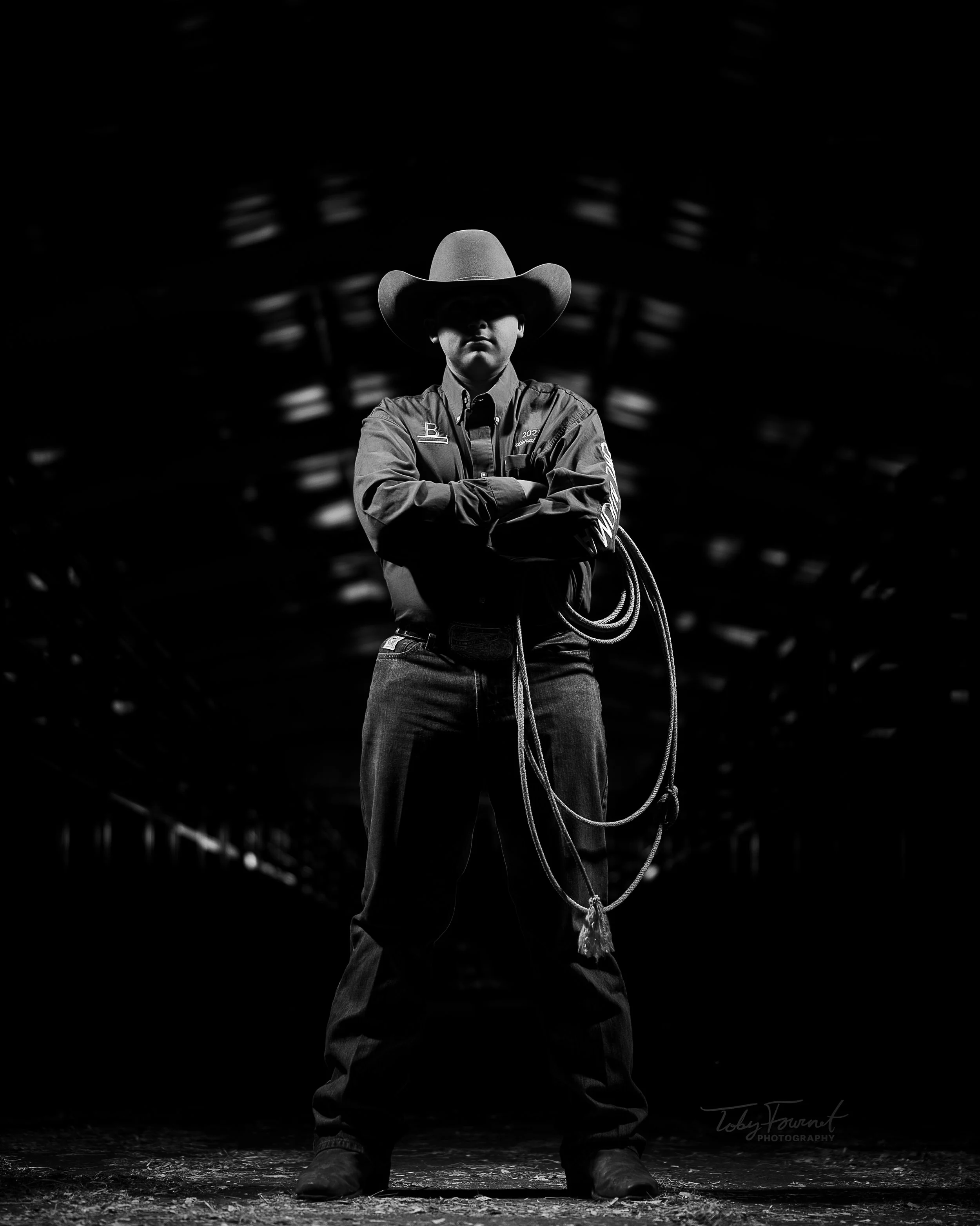 Black-and-white portrait of a cowboy holding a rope in a barn