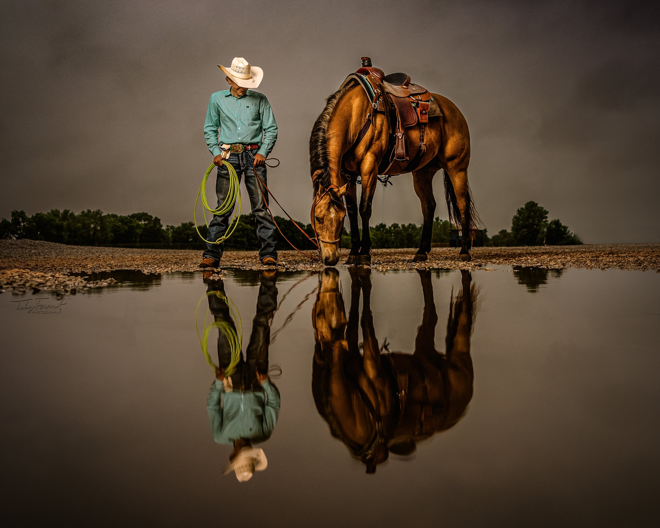 Cowboy and saddled horse reflected in a pool of water