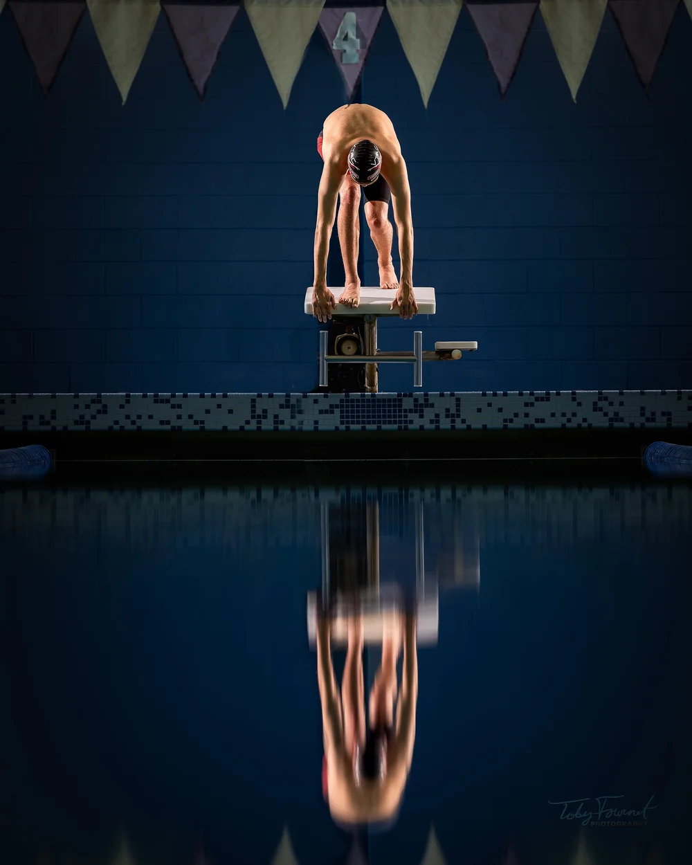 Senior swimmer on a starting block reflected in the pool