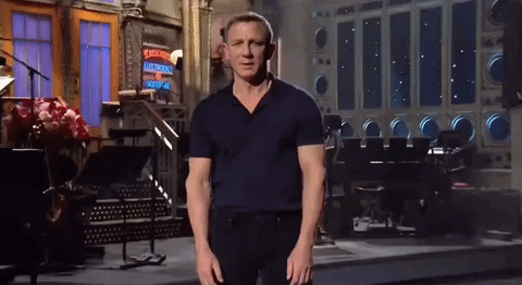 New James Bond (Daniel Craig, a stunning white man in a black shirt and pants) stands on the stage introducing The Weekend.