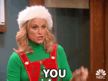 A blonde woman in a red elf outfit points at someone and says YOU