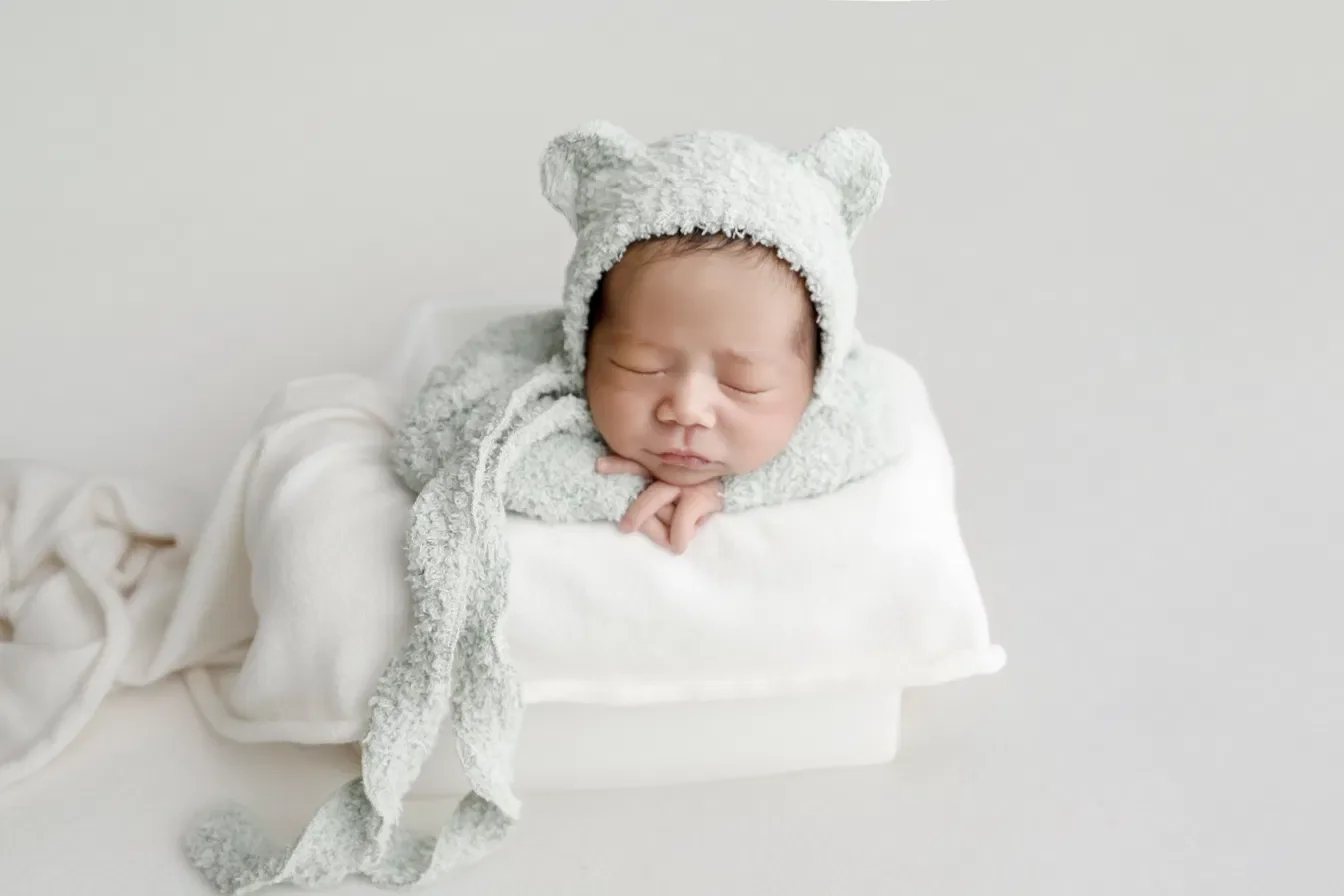 Newborn in a lavender ruffled wrap posed in a lilac bucket with purple florals on a floral backdrop