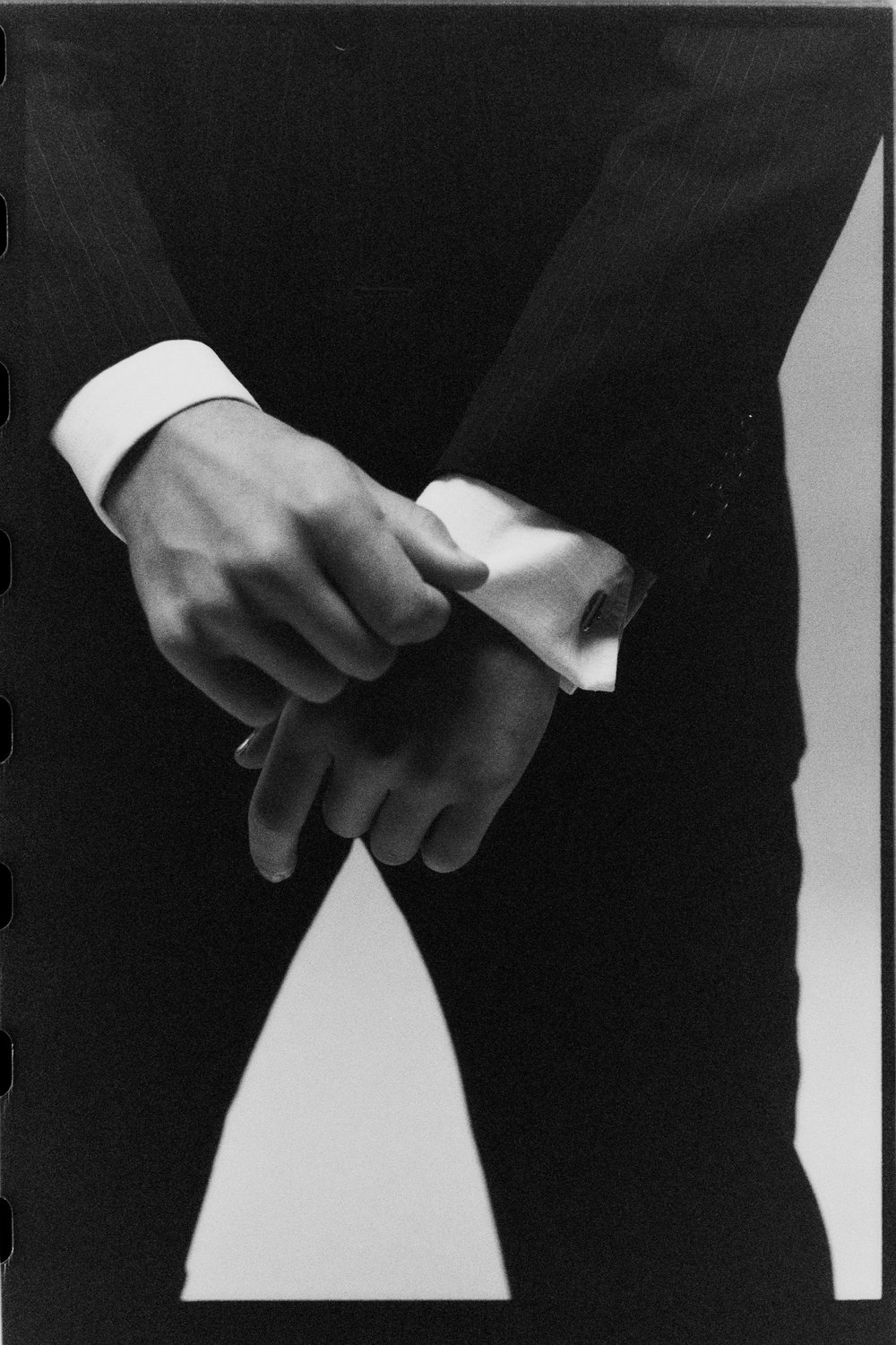 Hands wringing a shirt cuff against a dark suit