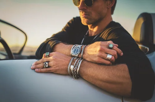 Close-up of Buck Palmer men's turquoise and silver rings, stacked bracelets and dive watch on a classic Porsche convertible at golden hour