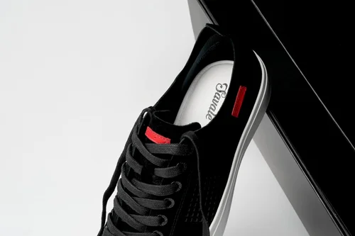 Close-up of the Savalé logo insole and red leather tab on a black suede sneaker, footwear detail photography