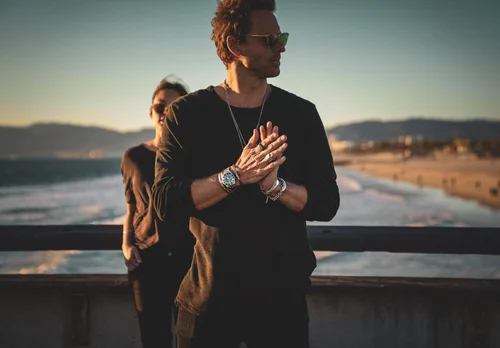 Buck Palmer wearing layered silver necklaces, rings and a dive watch on a Los Angeles beach pier at golden hour
