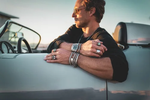 Close-up of Buck Palmer silver rings and stacked bracelets on a man's arms resting on a classic Porsche convertible