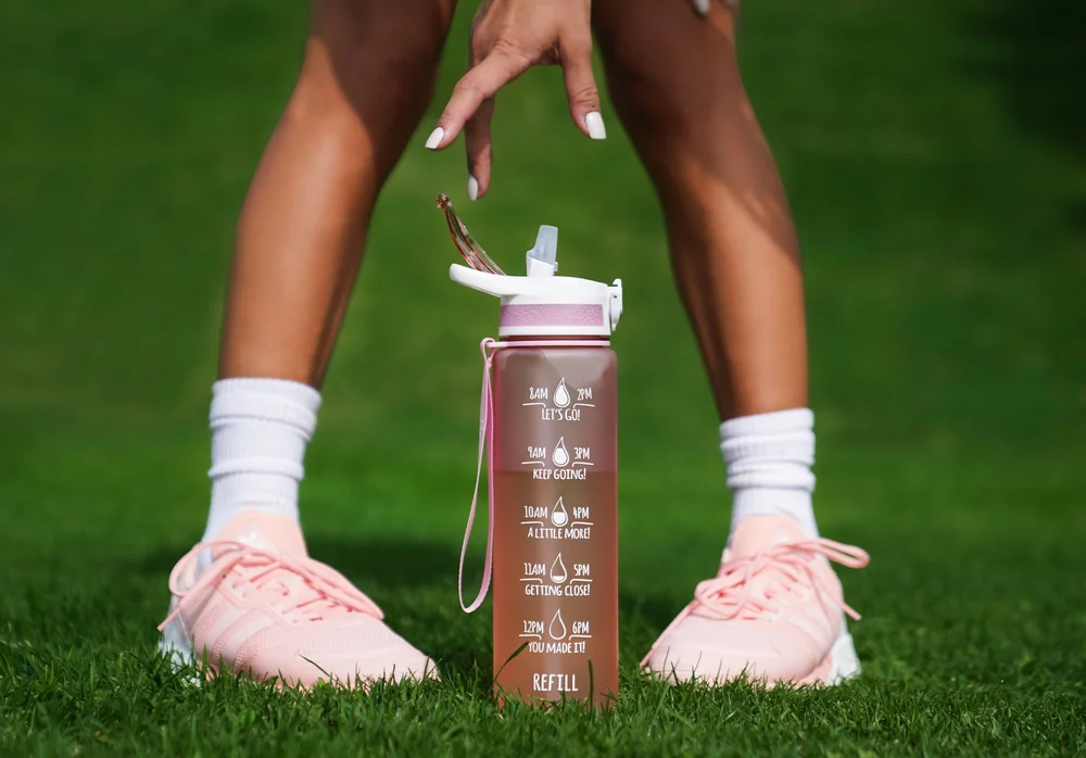 Athlete in pink sneakers grabbing a pink fitness water bottle on green turf