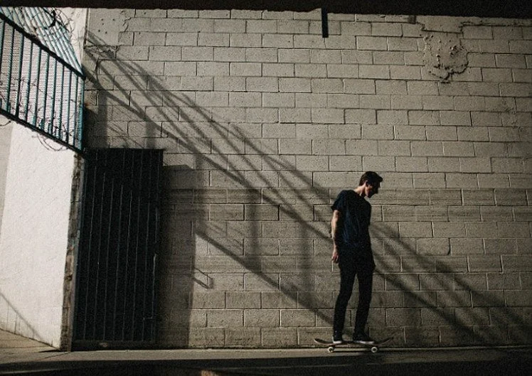 Skater rolling past a sunlit cinder block wall in downtown Los Angeles, menswear footwear lifestyle campaign