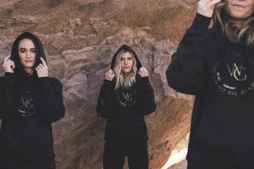 Three models holding up the hoods of black Women of the Galaxy logo hoodies against a sandstone wall