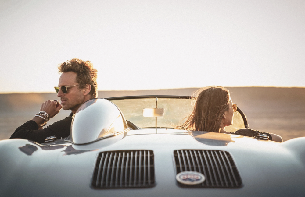 Man driving a vintage convertible along the coast wearing statement rings and a bracelet, shot for a premium men's jewelry campaign in Malibu