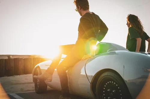 Man sitting on a classic silver Porsche convertible at sunset for a Buck Palmer men's jewelry lifestyle campaign