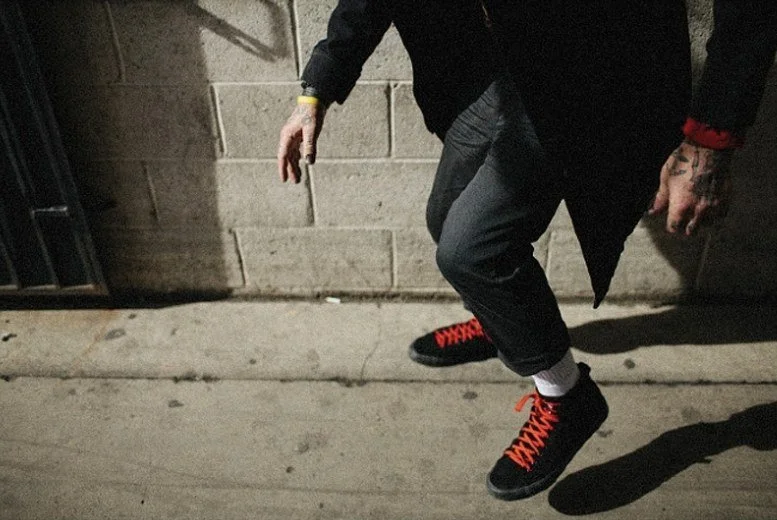 Close crop of black suede sneakers with red laces mid-step on a Los Angeles sidewalk